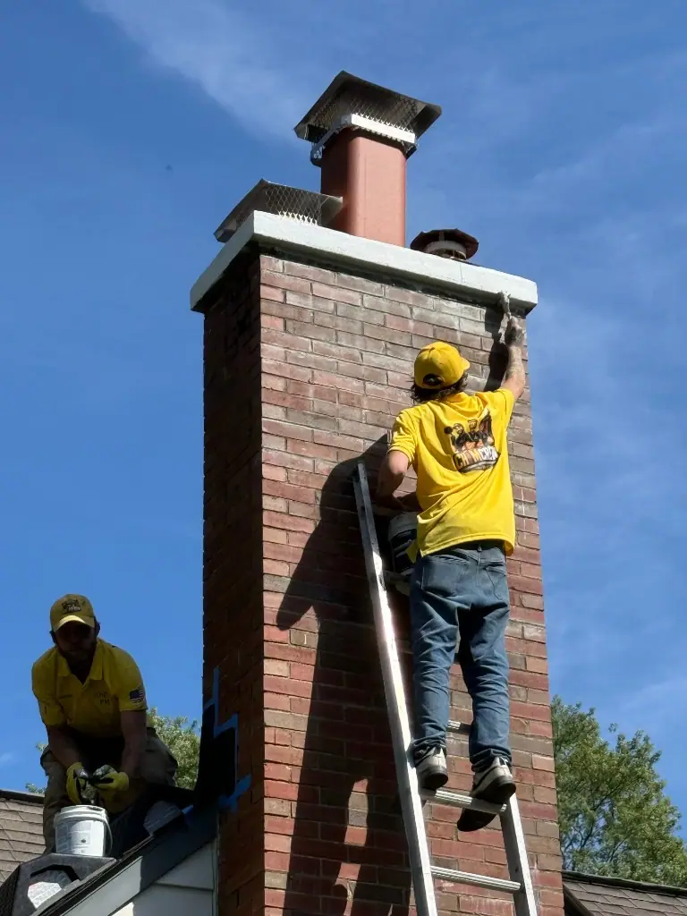 Chimcrew - Chimney Sweep & Repair techs in yellow uniforms finishing a dual-cap brick chimney from a ladder